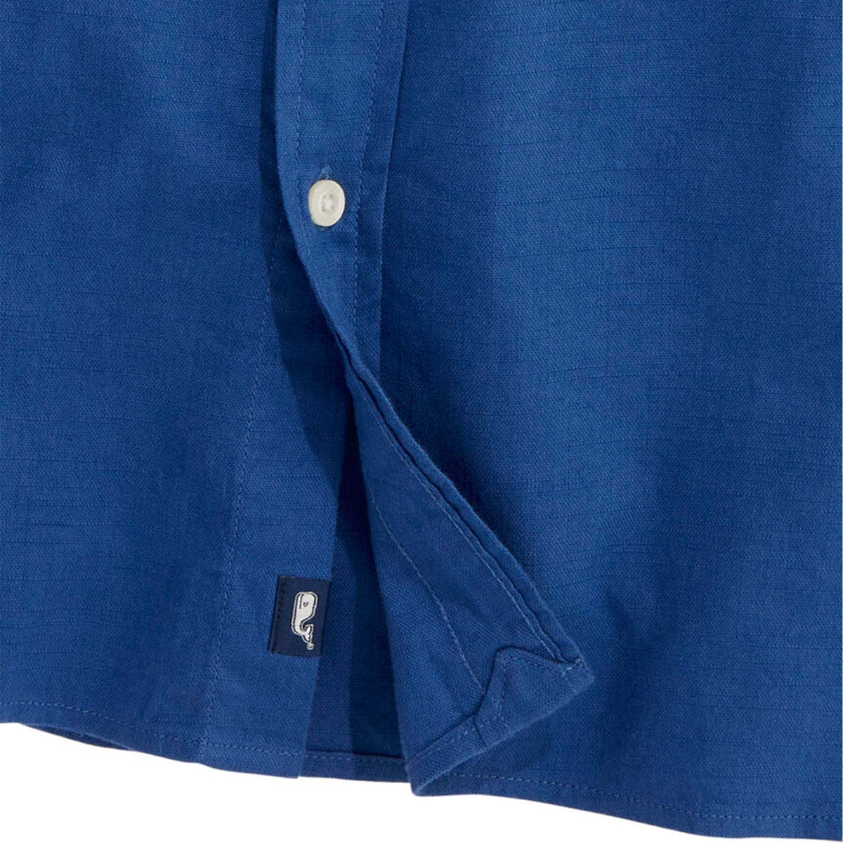 Close-up of shirt hem showing Vineyard Vines whale logo tag on solid Moonshine blue button-down.