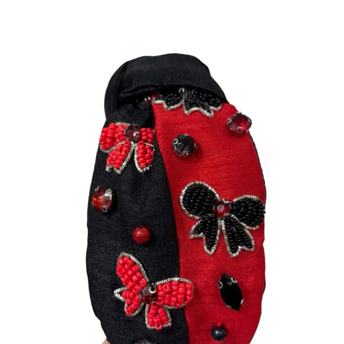 Top view of black and red knotted headband with beaded bow accents in red and black, decorated with gems and beads.