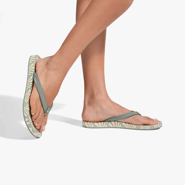 Person wearing green floral flip-flops on a white background