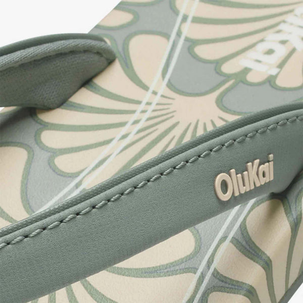Close-up of a green and beige Olukai sandal with floral pattern and brand name.