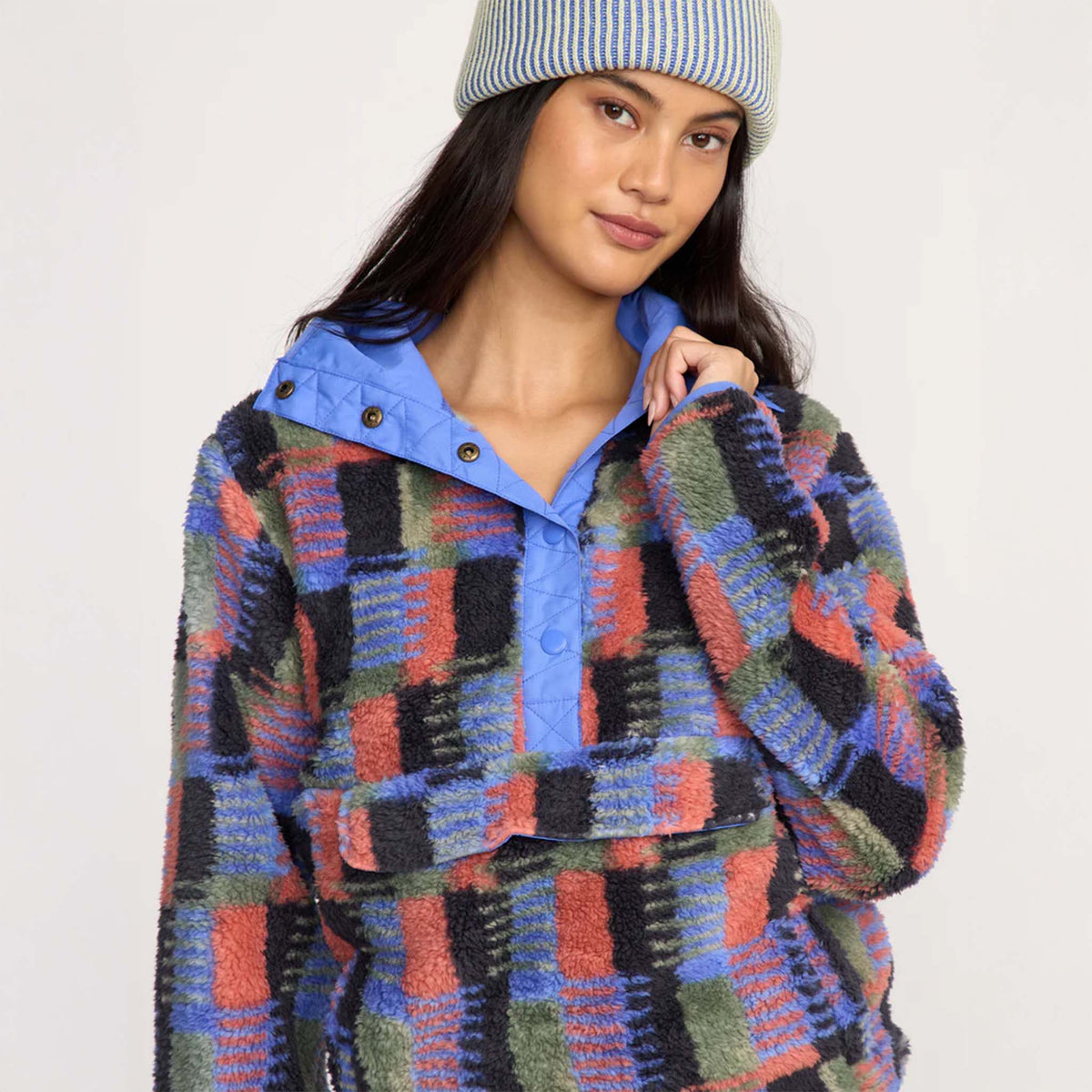 Woman wearing multicolor plaid sherpa pullover with blue collar, lightly pulling at neckline to show snap detail.