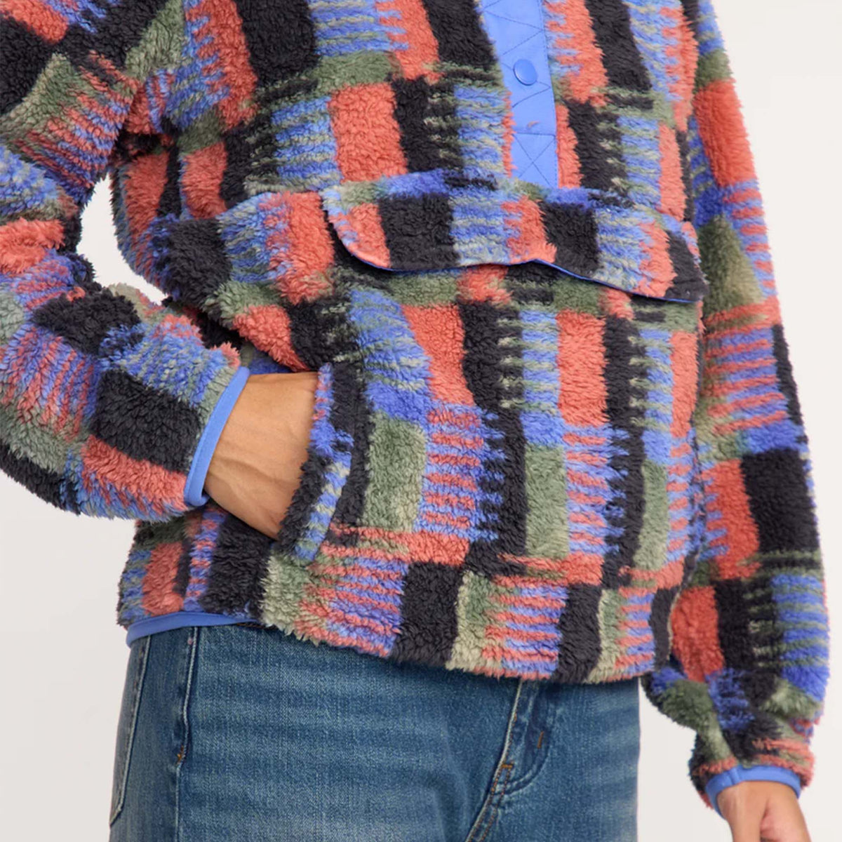 Close-up of multicolor plaid sherpa pullover showing front flap pocket and hand tucked in side pocket.