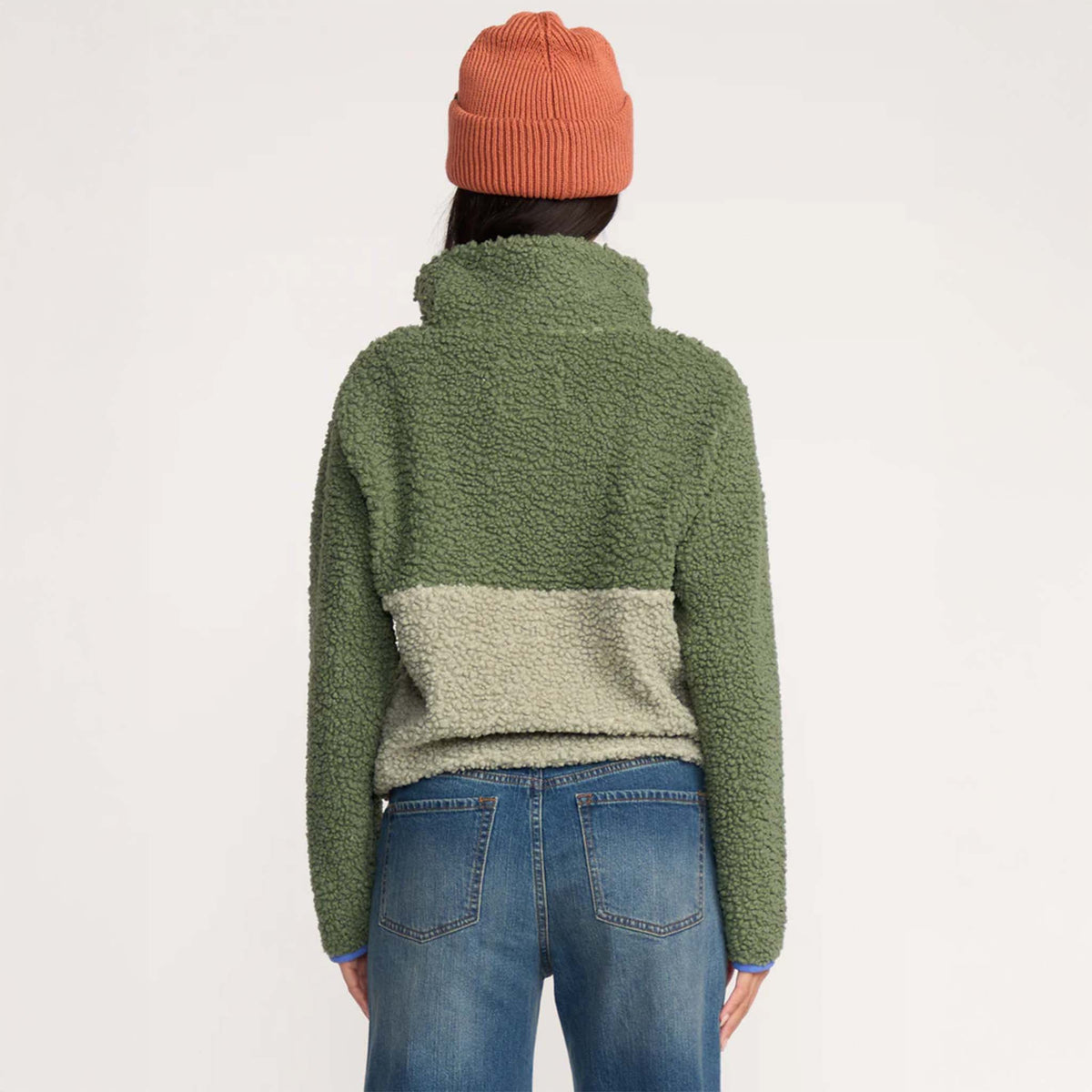 Back view of woman wearing two-tone green sherpa pullover showing contrast panel design and high collar.