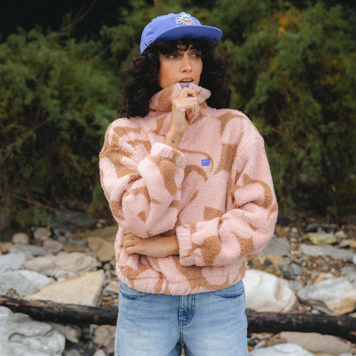 Outdoor shot of woman wearing pink and tan sherpa pullover with blue zipper and jeans.
