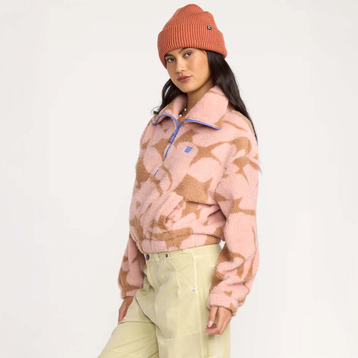 Side view of woman wearing pink and tan sherpa pullover with blue zipper and beanie.
