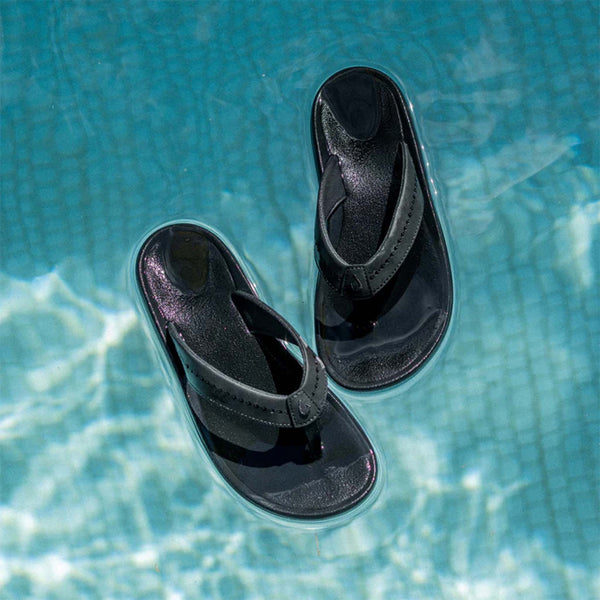 Black Olukai sandals floating in clear blue water