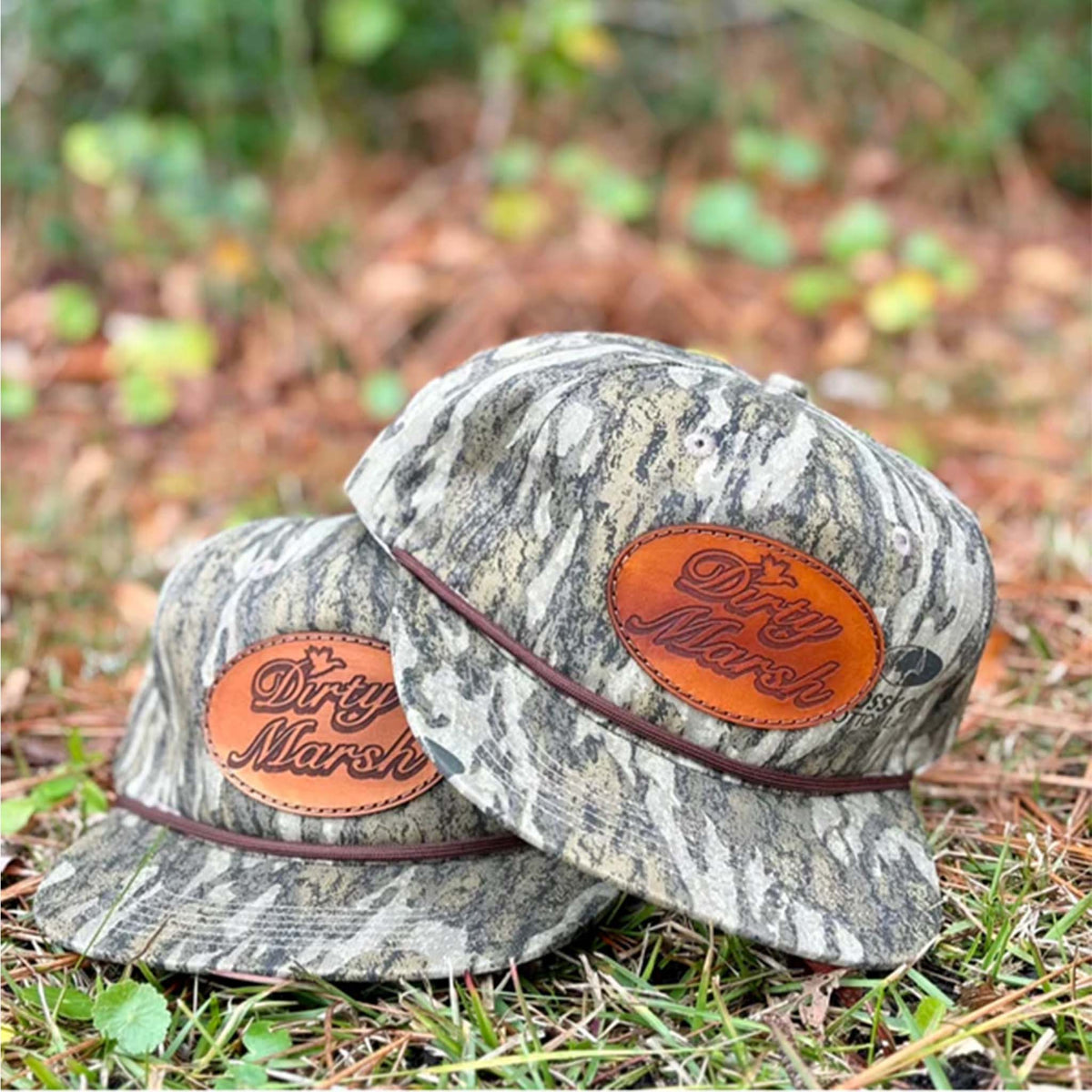 bottomland camo hat with a leather patch featuring the dirty marsh logo on the crown.  brown rope stretched across the bill.