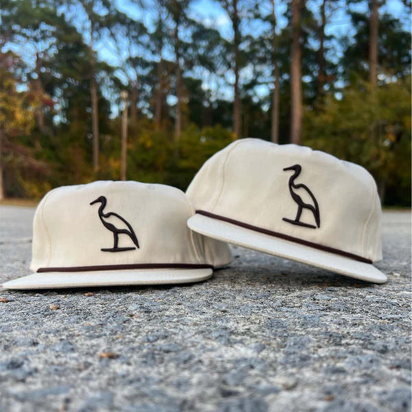 Cream colored hat with brown embroidered heron on the crown and rope stretched across the bill.