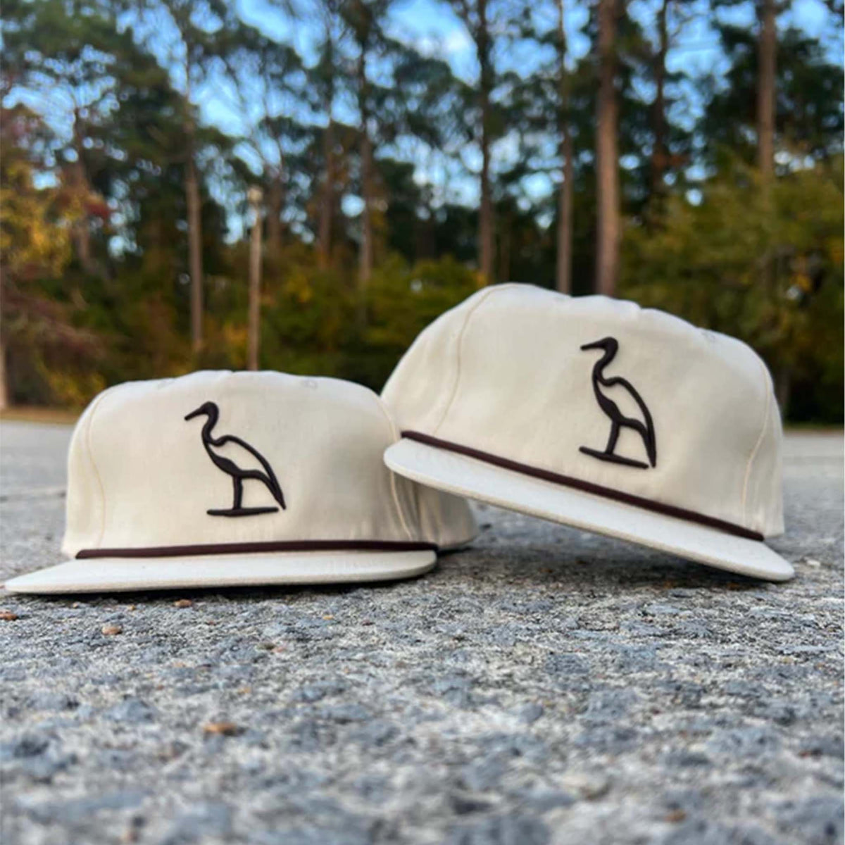 Cream colored hat with brown embroidered heron on the crown and rope stretched across the bill.
