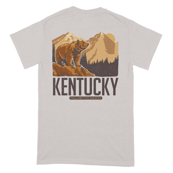  Back of light gray short sleeve t-shirt with brown bear graphic, mountain background, and large “Kentucky” text.
