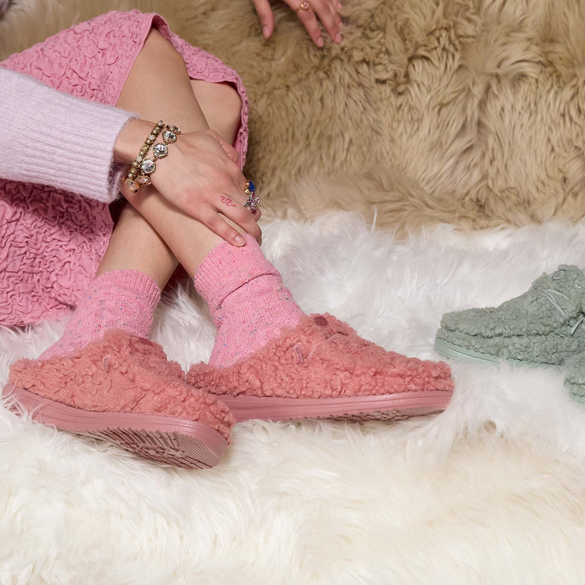 Person wearing pink fuzzy slippers on a fluffy white rug with a beige rug in the background.