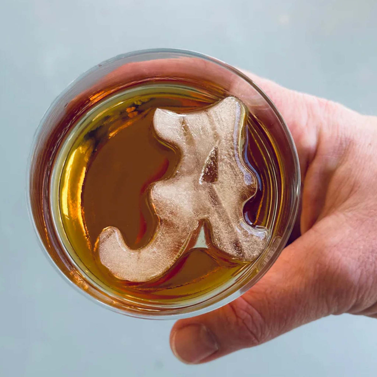 Close-up of Alabama scripted "A" ice cube floating inside a whiskey glass.