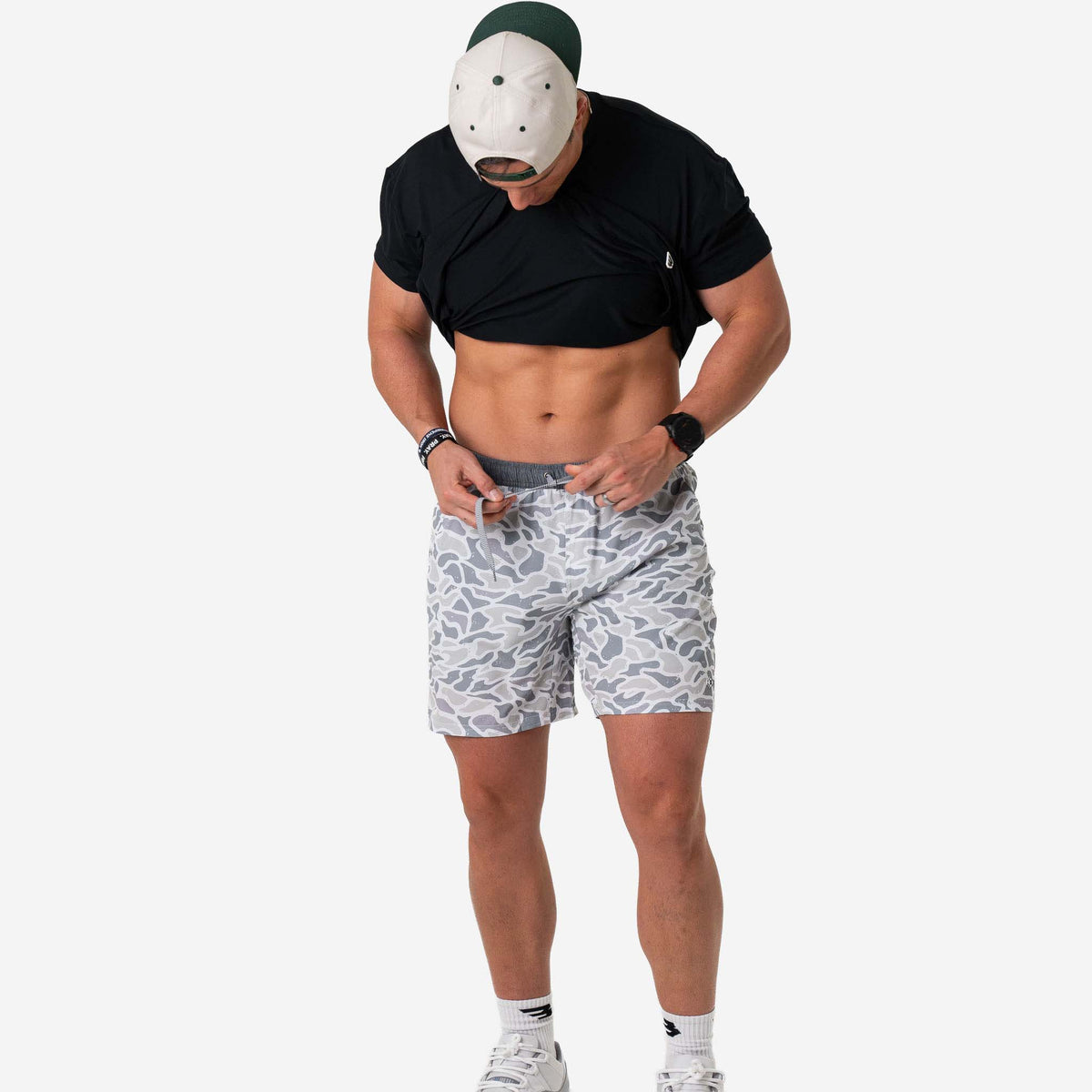 Person wearing a black t-shirt, patterned shorts, and a white mask on a white background