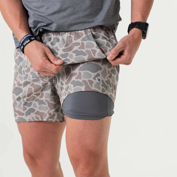 Man wearing deer camo athletic shorts with the top layer exposing a grey compression layer underneath.