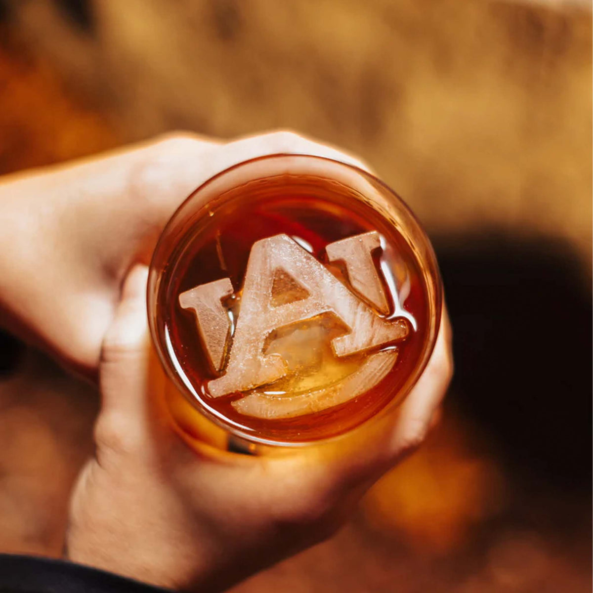 Close-up of clear Auburn University logo-shaped ice cube inside a glass of whiskey.