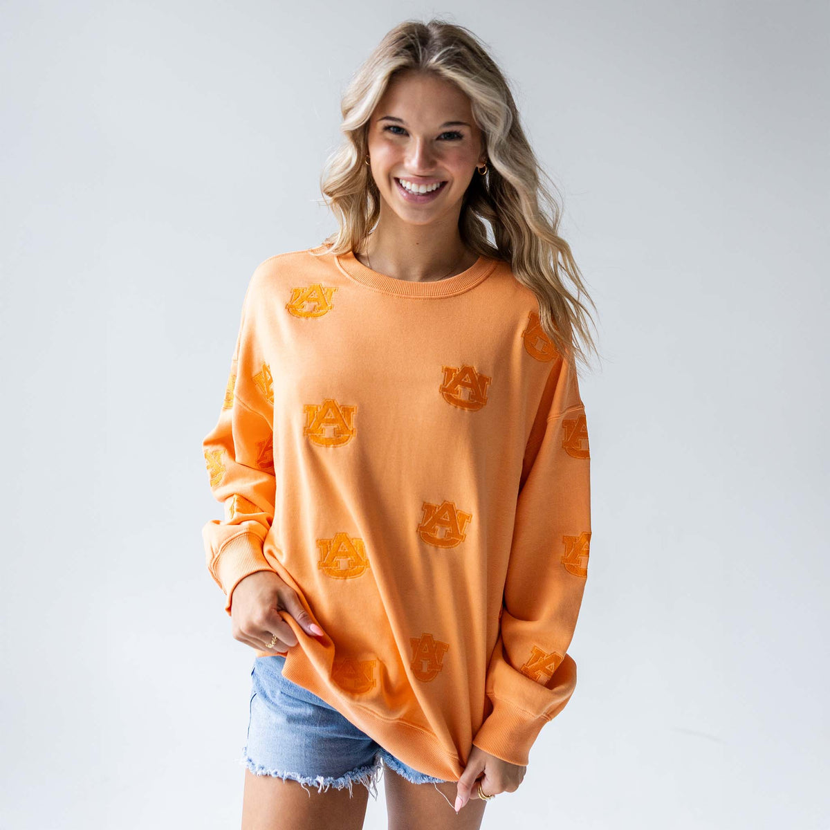 Front view of woman wearing an oversized orange sweatshirt with allover tonal Auburn University logos