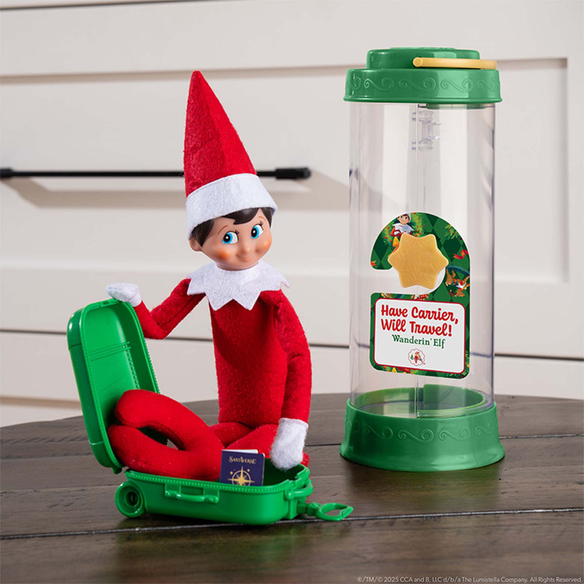 Elf on the Shelf with travel carrier and suitcase on a wooden surface
