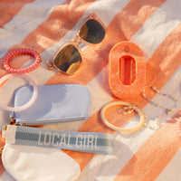 Collection of accessories including sunglasses, hair ties, and a pouch on a striped fabric background