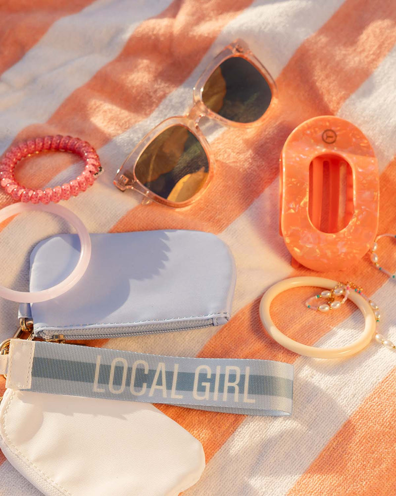 Assorted accessories including sunglasses, wristlet pouch, hair ties, and keychain arranged on striped towel.