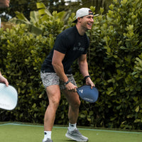 A man in athletic gear holding a pickleball paddle, smiling.