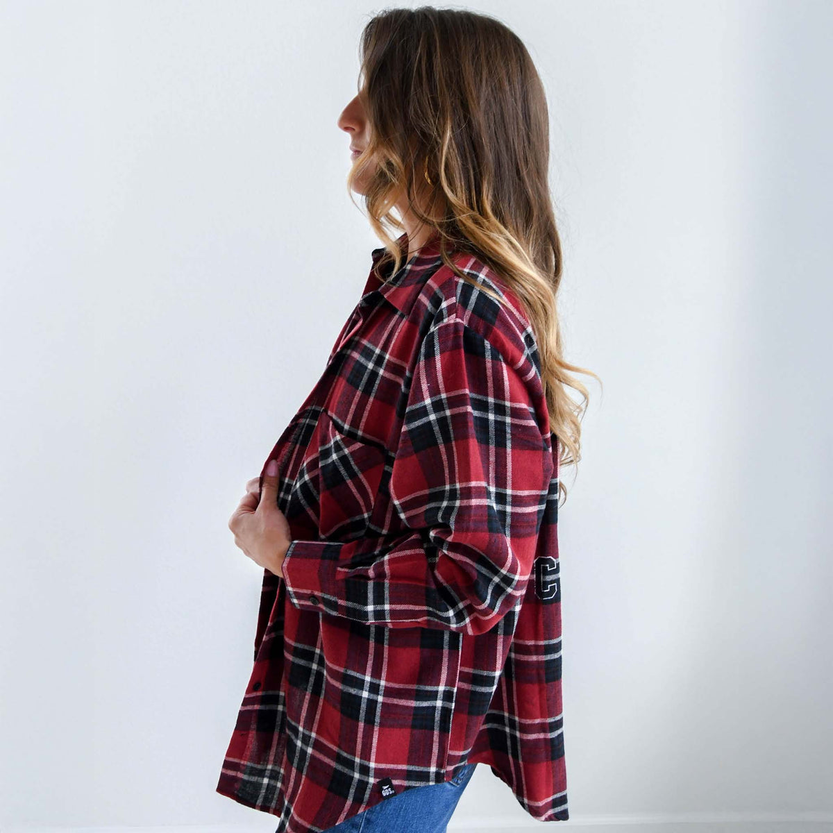 Side profile of woman wearing red and black plaid flannel shirt, holding front edges with one hand.