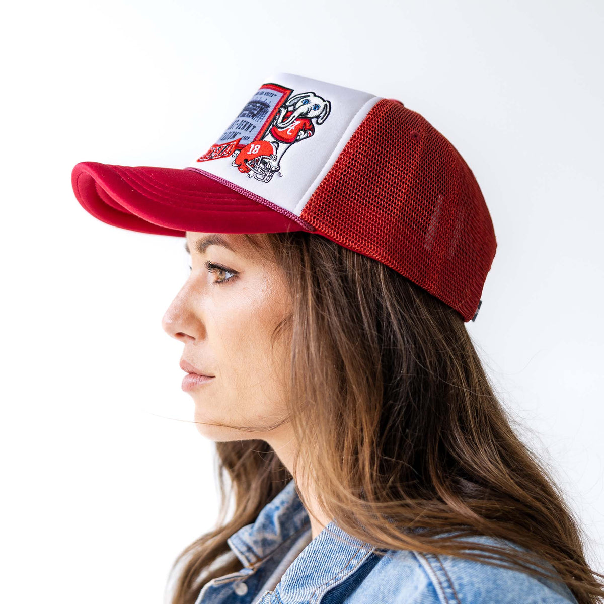 Woman wearing a Alabama football themed trucker hat with red mesh, adjustable snapback, and white foam crown with Bama themed patch collage style.