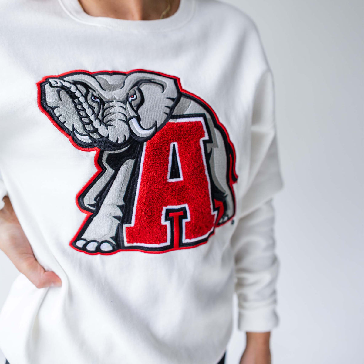 Close-up of white Alabama crewneck sweatshirt showing detailed chenille elephant and varsity “A” patch.