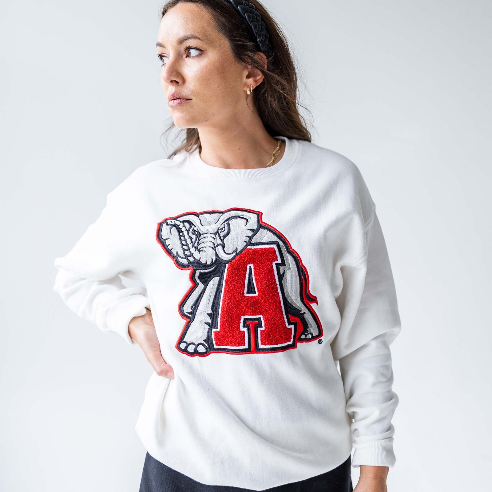 Woman wearing a white Alabama crewneck sweatshirt with large chenille elephant and varsity “A” patch on the front.