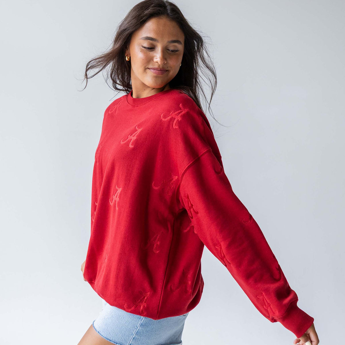 Woman in crimson crewneck sweatshirt with tonal Alabama “A” embroidery, turned slightly to the side.