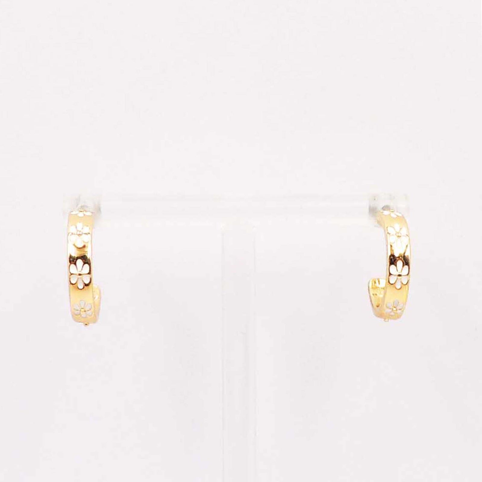 A pair of small gold-tone hoop earrings displayed on a clear stand, each featuring a row of white enamel daisy flower designs on the outer surface.