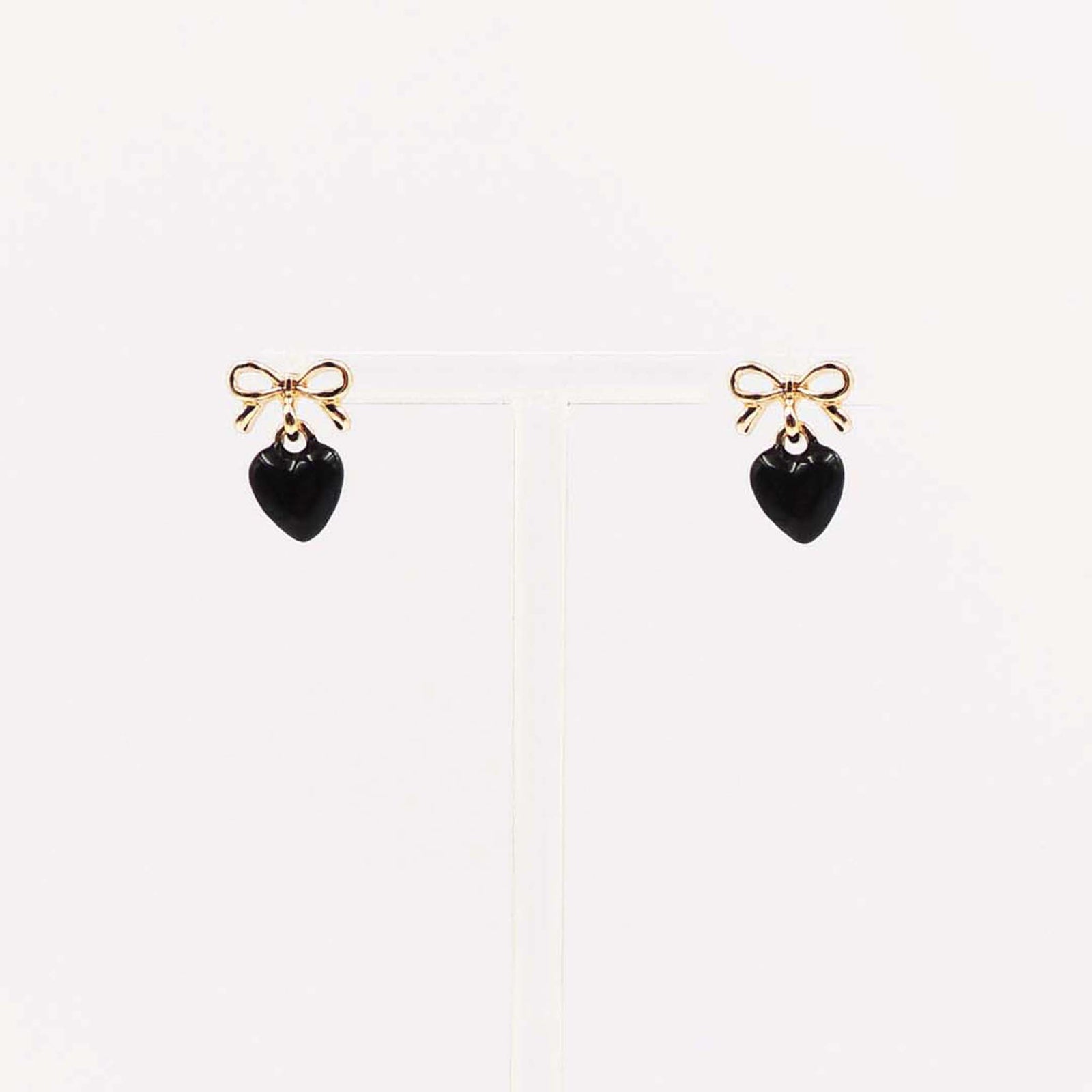 Gold bow stud earrings with dangling black enamel heart charm.
