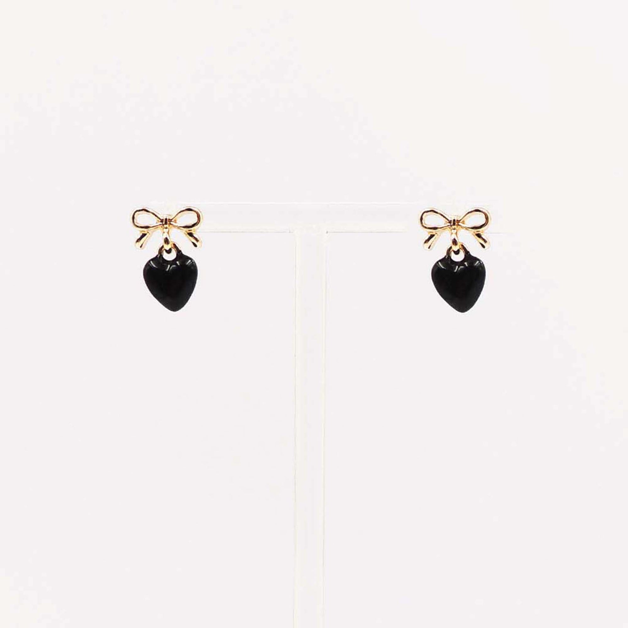 Gold bow stud earrings with dangling black enamel heart charm.