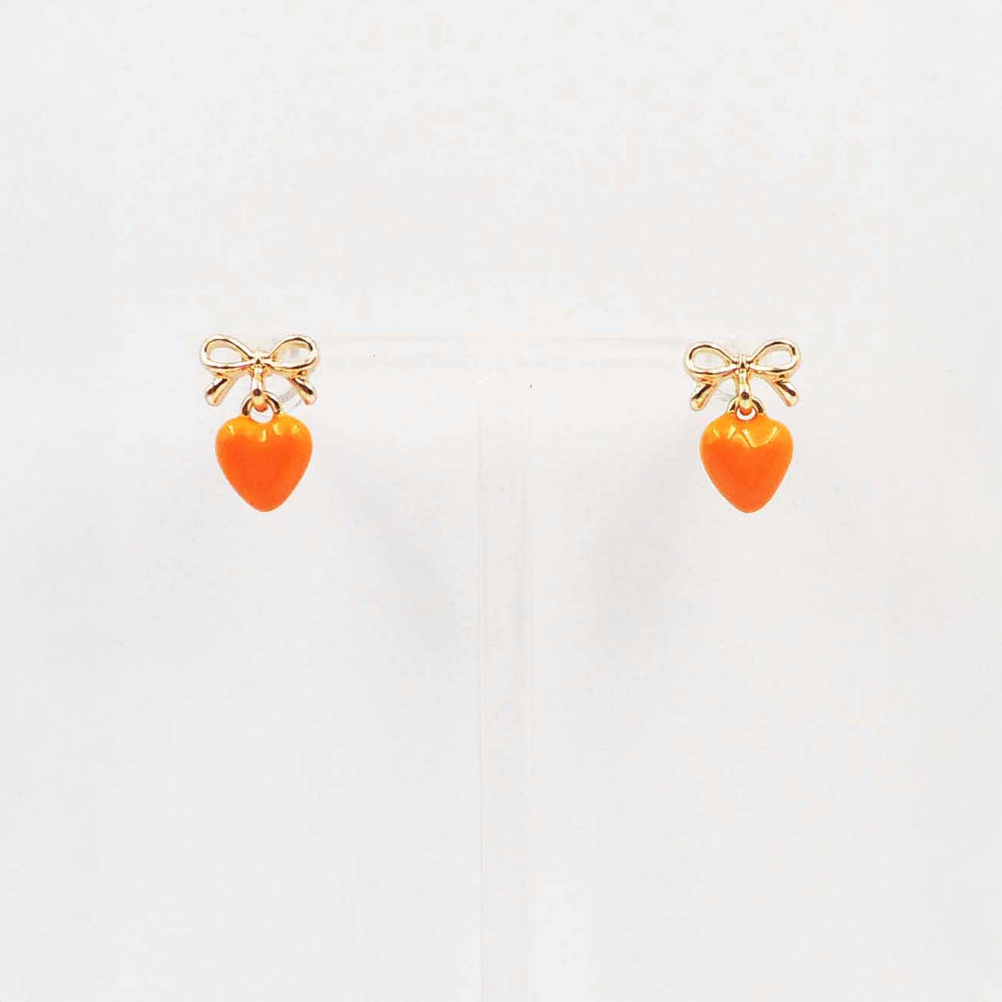 Gold bow stud earrings with dangling orange enamel heart charm.