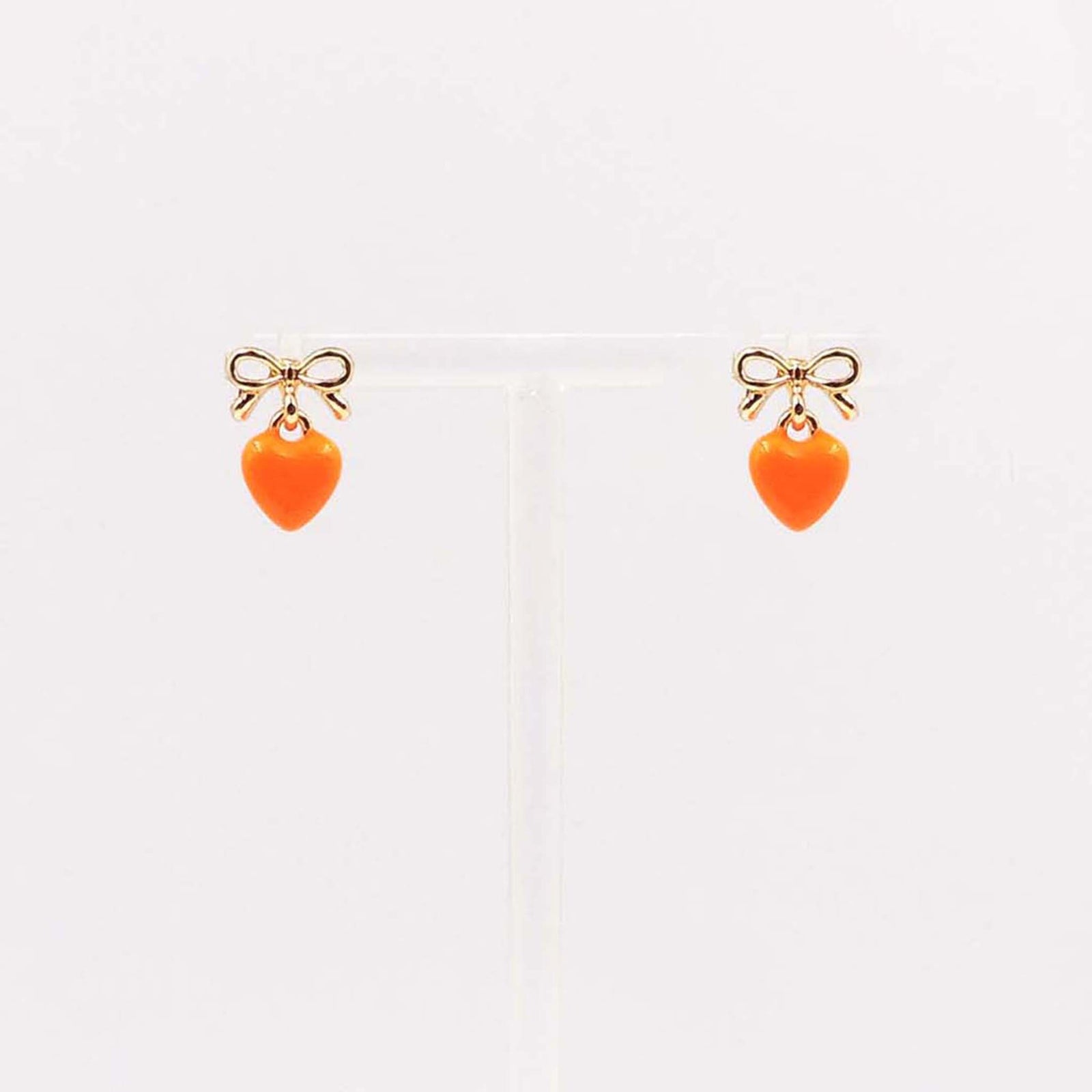 Gold bow stud earrings with dangling bright orange enamel heart charm.