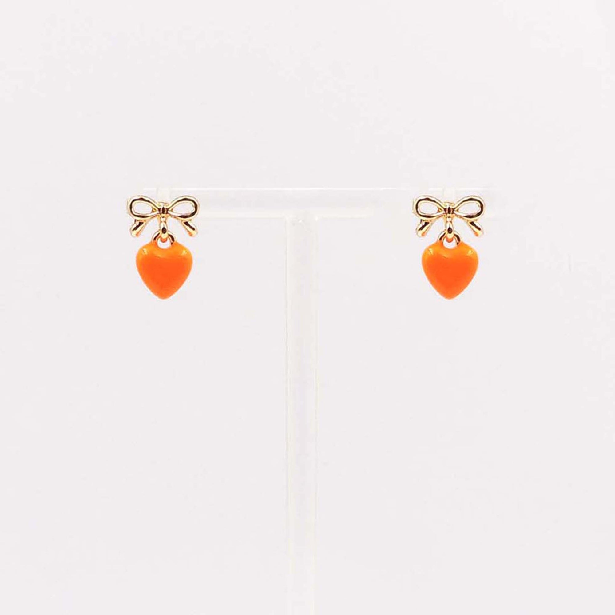 Gold bow stud earrings with dangling bright orange enamel heart charm.