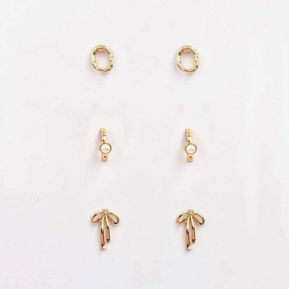 Alt text: Three-piece gold earring set featuring textured oval studs, pearl-accent huggies, and gold bow studs displayed on a card.