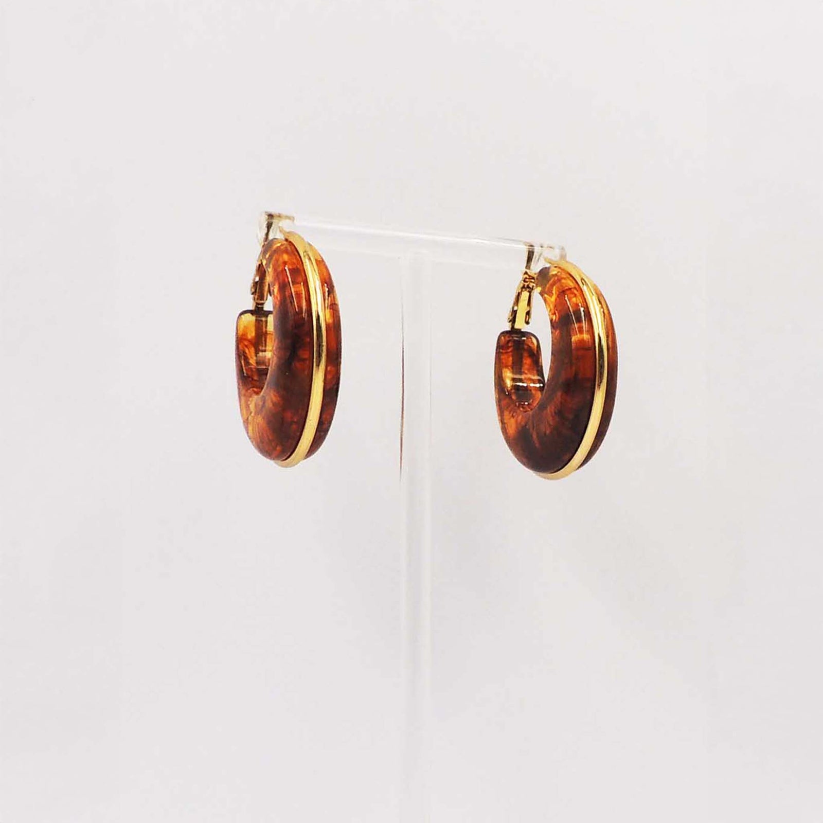 Pair of round tortoise-pattern hoop earrings with gold-tone edges displayed on a clear stand.