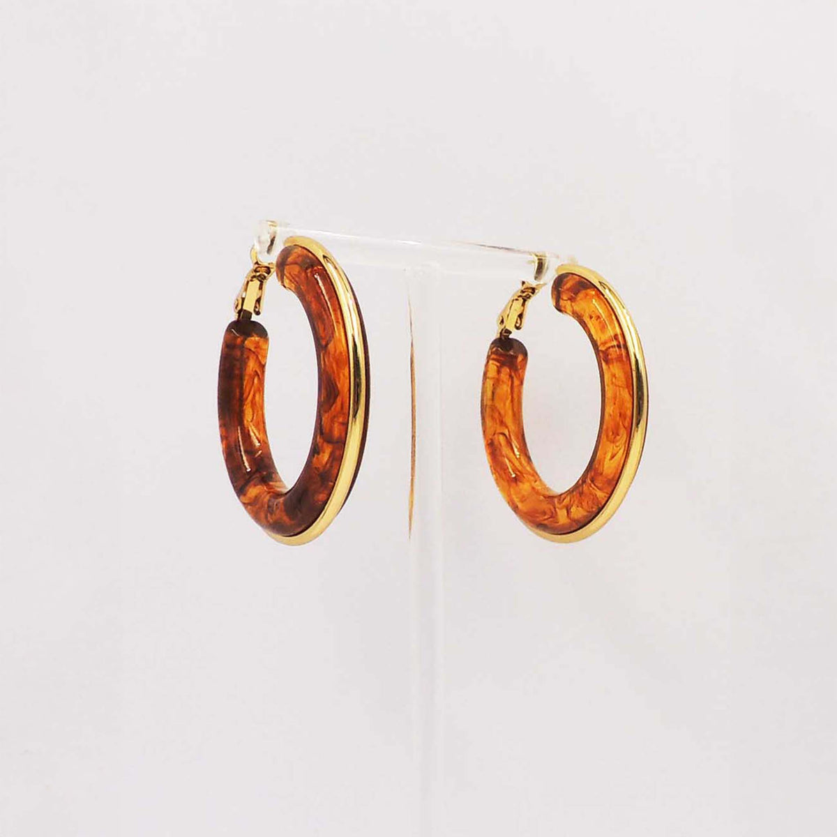 Pair of medium hoop earrings with tortoise shell pattern and gold-tone trim displayed on a clear stand.
