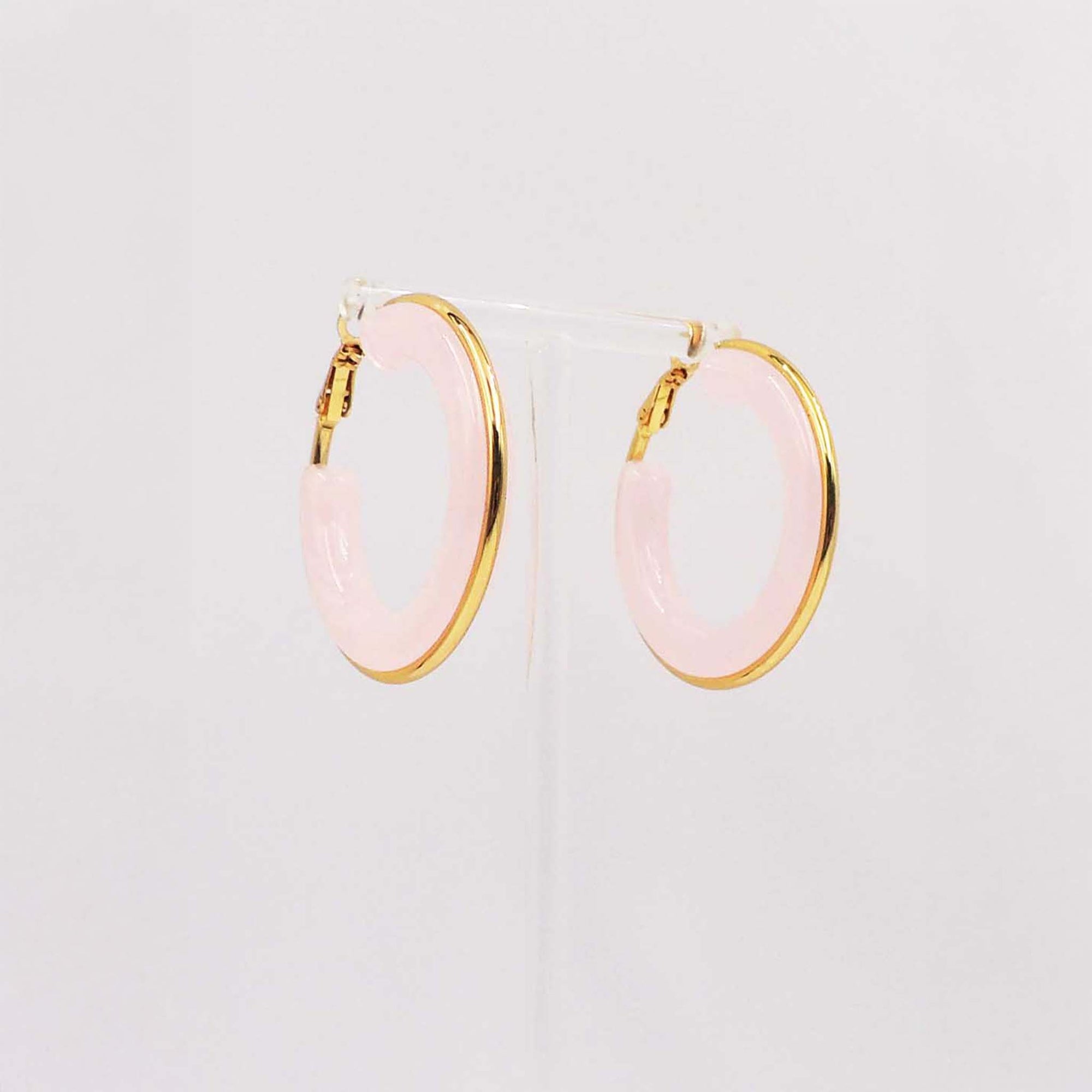 Pair of pastel pink hoop earrings with gold-tone edges displayed on a clear stand.