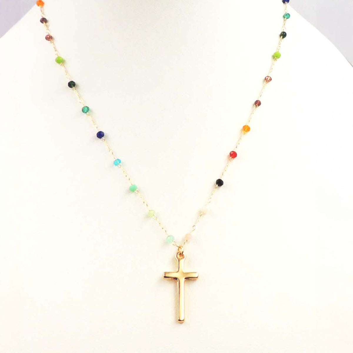 Gold cross pendant necklace with multi-colored beaded chain on white display stand.