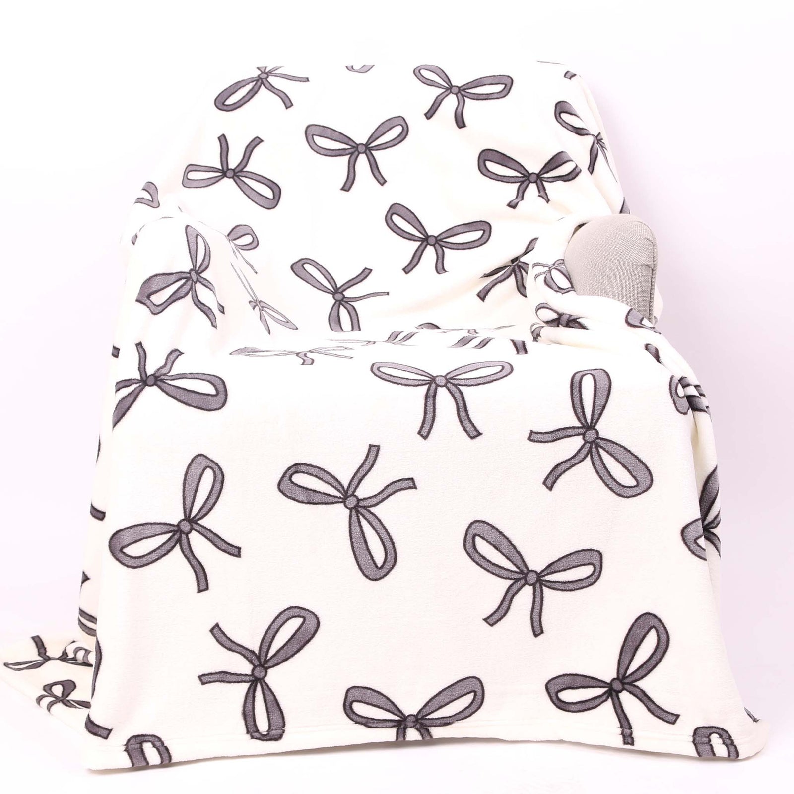 Palmetto Moon cream micro plush throw blanket draped over a chair, decorated with an allover black bow design.