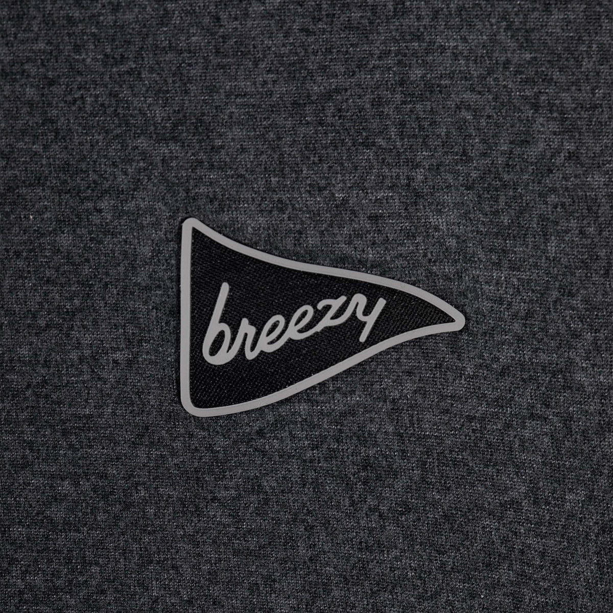 Close-up of Breezy logo patch in gray and black on pullover fabric.