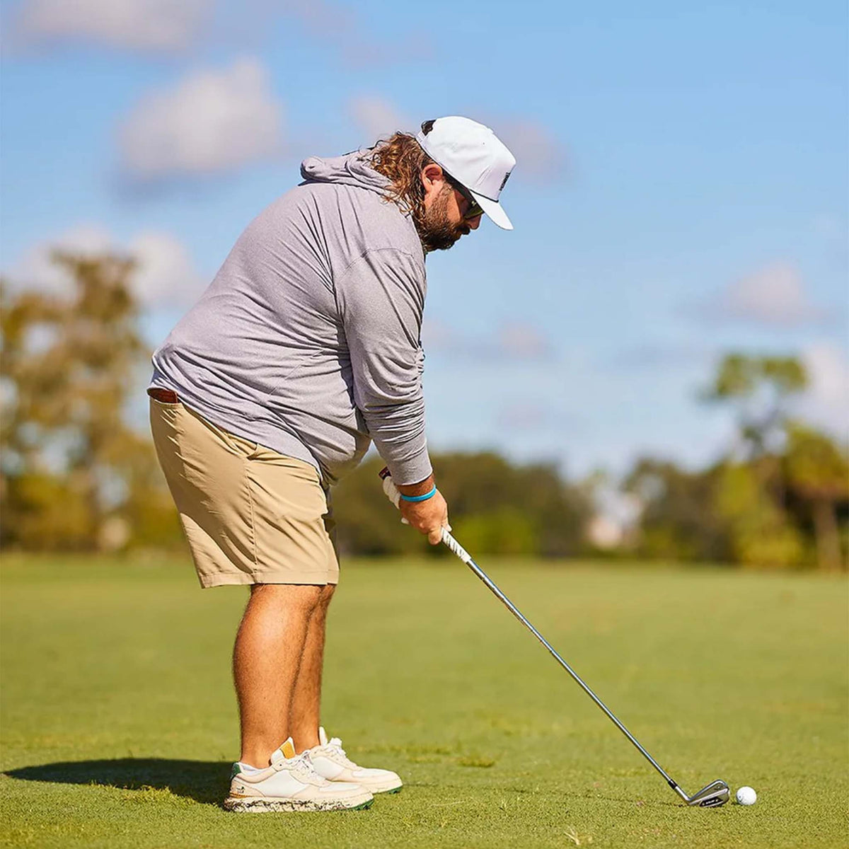 Lifestyle image of man golfing while wearing Breezy grey hoodie with khaki shorts and white cap.