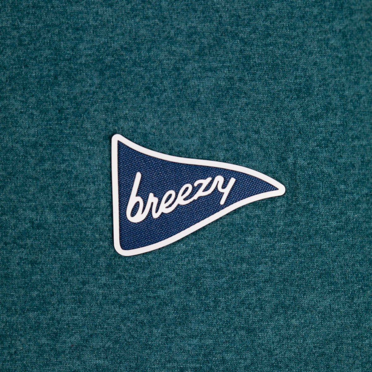 Close-up of Breezy quarter-zip pullover in forest green with a navy pennant logo patch reading "breezy" on the chest.
