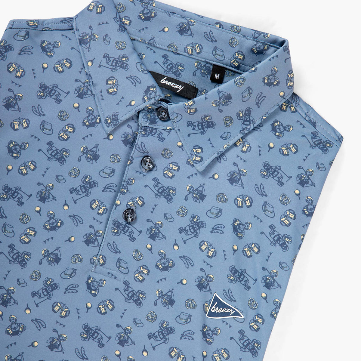 Breezy blue polo shirt with Oktoberfest-themed print featuring pretzels, beer mugs, sausages, and golfers. Folded with buttons and logo visible.