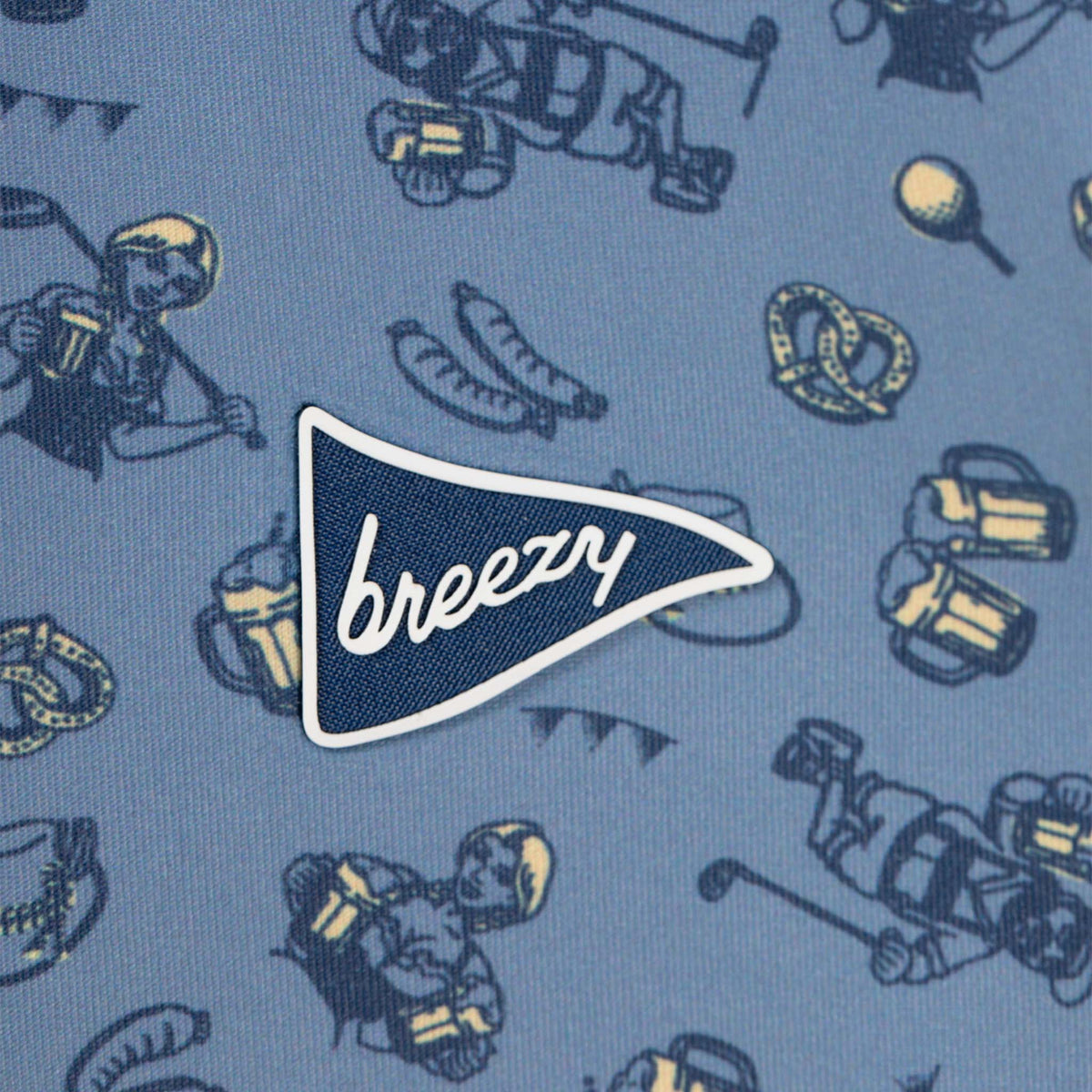 Breezy pennant logo on blue polo shirt with Oktoberfest-themed print of pretzels, beer mugs, sausages, and golfers.