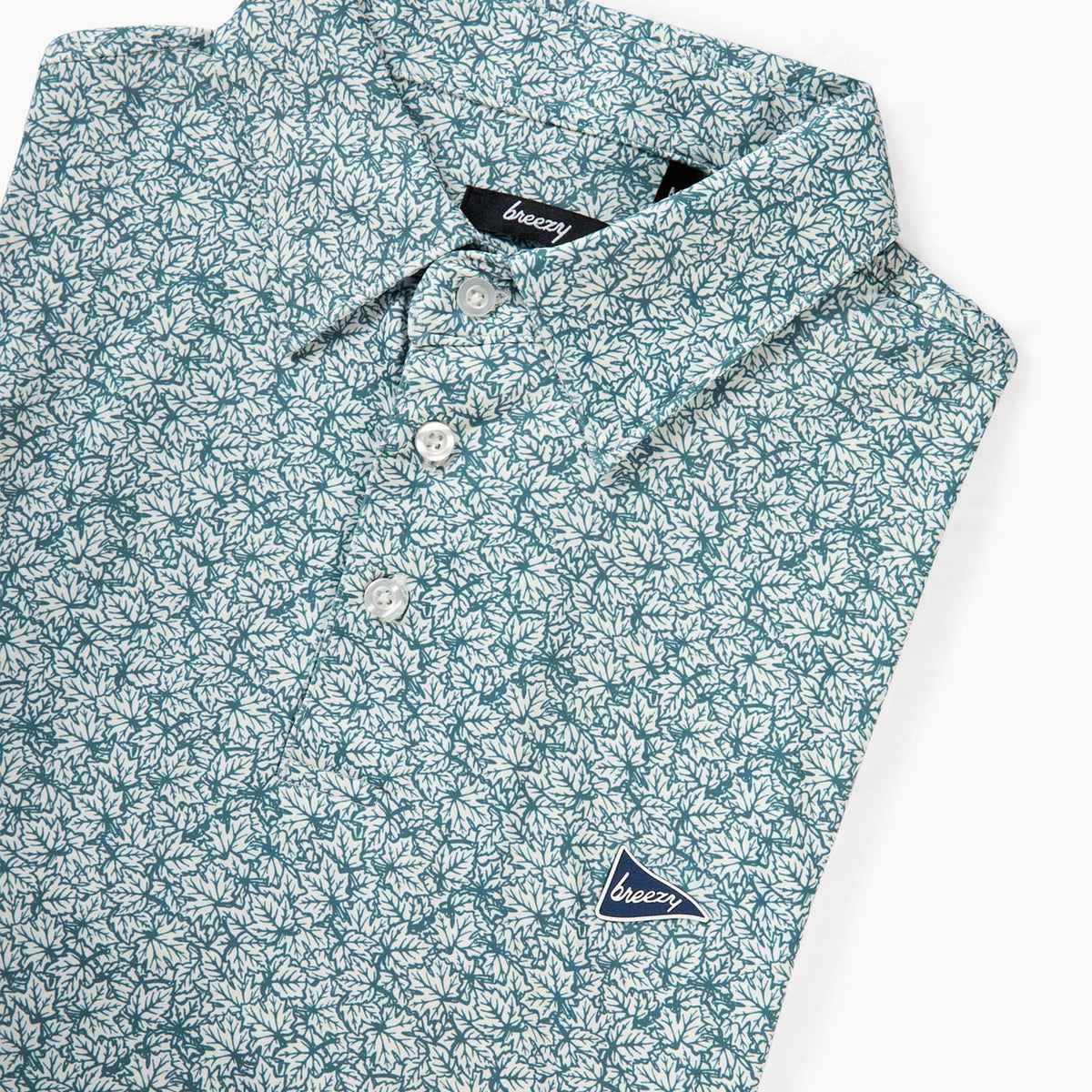 Breezy men’s performance polo in white and green leaf print folded at an angle showing button placket and logo detail on chest.