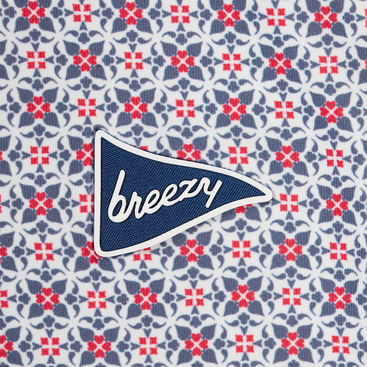 Close-up of Breezy RWB patterned polo fabric showing geometric red and navy floral motifs on white background with Breezy pennant logo.