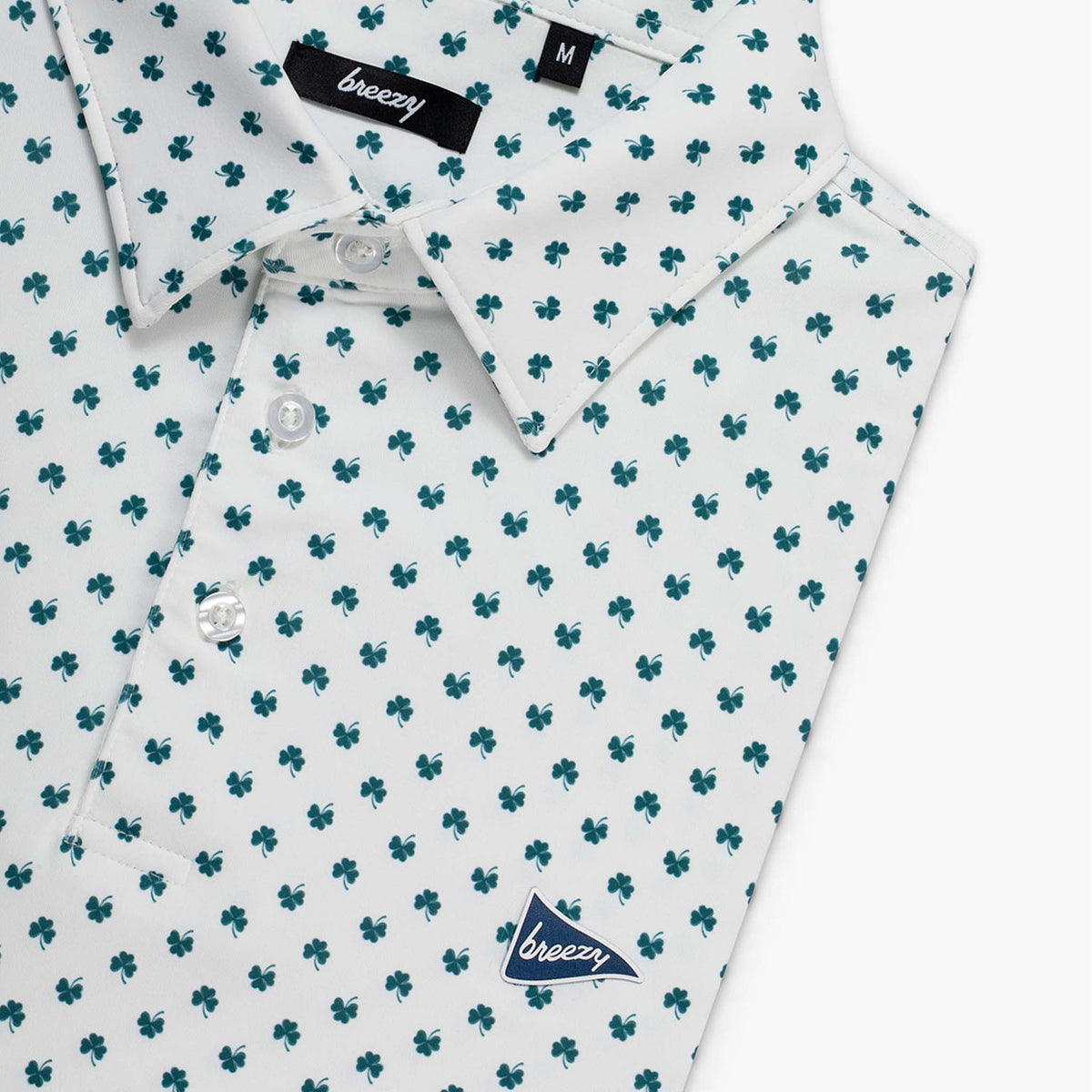 Folded white polo shirt with green clover pattern and 'Breezy' branding shown on a white background