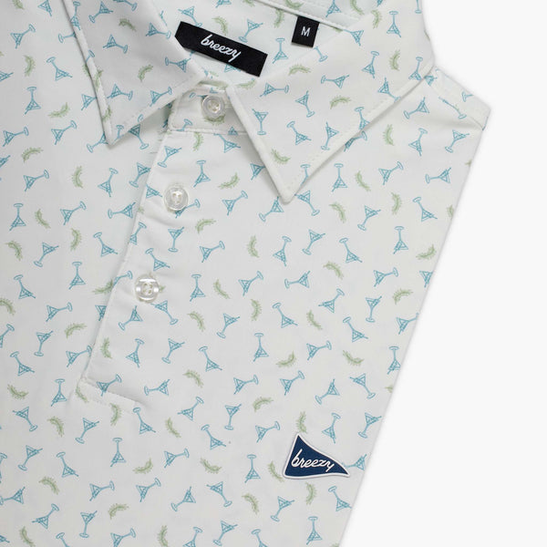 Folded men's white polo with an all over print of small martini glasses in blue and green shown on a white background